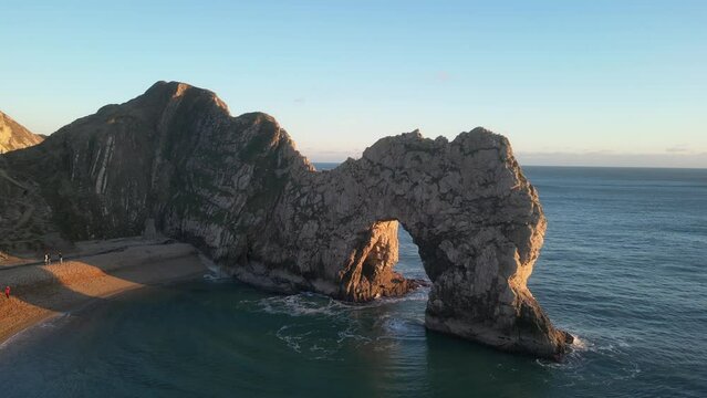 The sun goes down on the Jurassic coast and Durdle Door in Dorset with Seak Pink Trift growing on the top of the cliff in the foreground. Durdle Door, Dorset, Jurassic Coast, England, UK