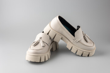 Trendy fashionable beige leather   women pair platform loafers on neutral grey background. Casual spring or summer comfort style.
