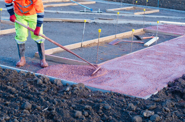 Builders pouring and leveling wet ready-mix concrete into formwork   during new footpath...
