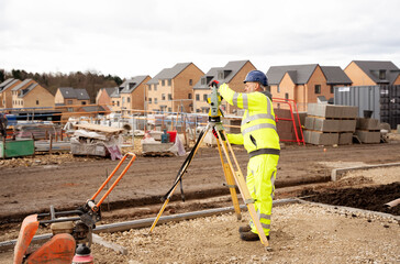 Surveyor builder site engineer with theodolite total station at construction site outdoors during surveying work