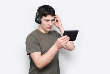College student, young guy studying online, looking at tablet and fixing wireless headphones, guy looking at tablet in concentration, online education