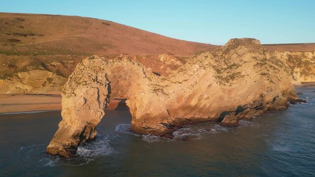 The sun goes down on the Jurassic coast and Durdle Door in Dorset with Seak Pink Trift growing on the top of the cliff in the foreground. Durdle Door, Dorset, Jurassic Coast, England, UK