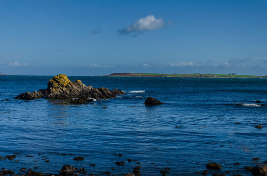 Gentle waves lapping the rocks at Co Down coast nearGroomsport with blue sky and sea and Copeland Island in the distance