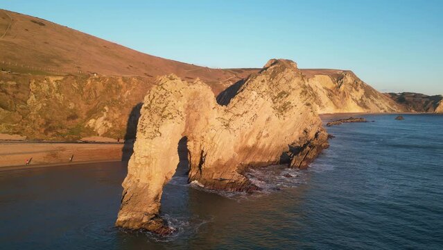 The sun goes down on the Jurassic coast and Durdle Door in Dorset with Seak Pink Trift growing on the top of the cliff in the foreground. Durdle Door, Dorset, Jurassic Coast, England, UK