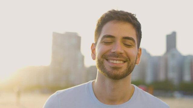 Handsome man looking at camera. Closeup positive guy smiling at camera. Portrait of male model posing on camera in urban sunset background. Cheerful man face with positive emotion
