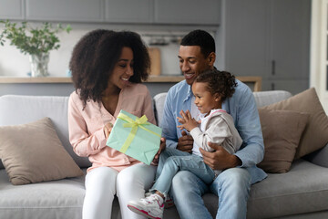 African american parents congratulating their little daughter, celebrating birthday holiday, giving...