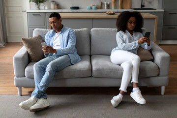 Indifference concept. Black couple using mobile phones sitting on different sides of couch, ignoring one another at home, full length - obrazy, fototapety, plakaty