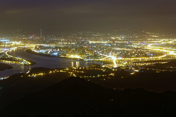 Aerial panorama of Taipei at night, the vibrant capital city of Taiwan, with view of bridges over Tamsui River, 101 Tower amid high rise buildings in downtown & bright city lights dazzling in the dark