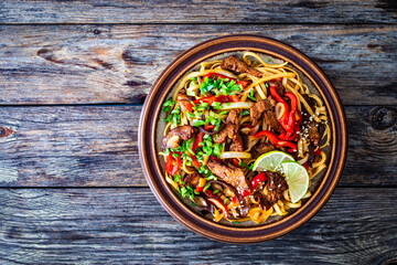 Asian style stir fried vegetables, roast beef and chow mein noodles on wooden table
