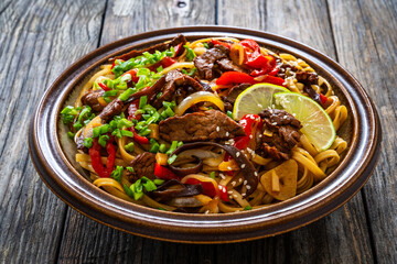 Asian style stir fried vegetables, roast beef and chow mein noodles on wooden table
