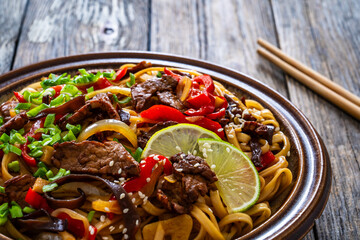 Asian style stir fried vegetables, roast beef and chow mein noodles on wooden table
