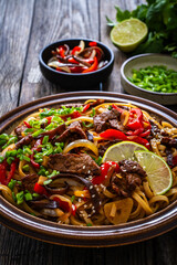 Asian style stir fried vegetables, roast beef and chow mein noodles on wooden table
