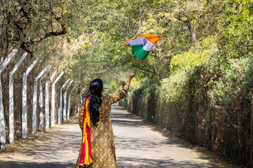 young girl waving the indian tricolor national flag at remote location at day from back angle