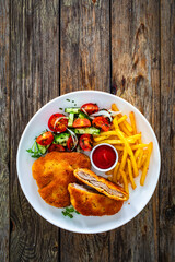 Crispy breaded fried pork loin chops with fries and fresh vegetables on wooden table
