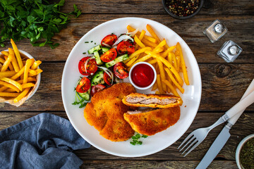 Crispy breaded fried pork loin chops with fries and fresh vegetables on wooden table

