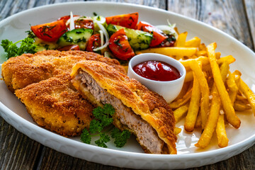 Crispy breaded fried pork loin chops with fries and fresh vegetables on wooden table
