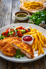 Crispy breaded fried pork loin chops with fries and fresh vegetables on wooden table
