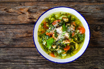 Pistou soup Nice - broth with basil pesto, bread, cheese and vegetables on wooden background in white bowl
