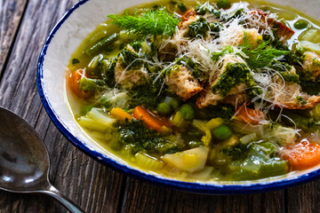 Pistou soup Nice - broth with basil pesto, bread, cheese and vegetables on wooden background in white bowl
