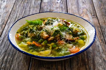 Pistou soup Nice - broth with basil pesto, bread, cheese and vegetables on wooden background in white bowl
