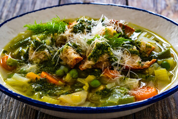 Pistou soup Nice - broth with basil pesto, bread, cheese and vegetables on wooden background in white bowl
