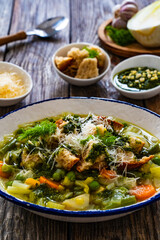 Pistou soup Nice - broth with basil pesto, bread, cheese and vegetables on wooden background in white bowl
