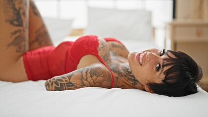 Hispanic woman with amputee arm wearing lingerie lying on bed smiling at bedroom