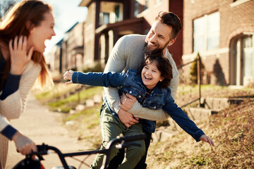 Family teaching child to ride bicycle in suburban neighborhood