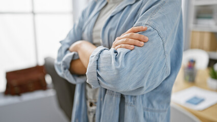 Beautiful blonde woman standing in office with arms crossed, oozing success as a young business professional.