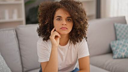 Young beautiful hispanic woman sitting on sofa with serious expression at home
