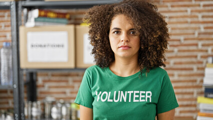 Young beautiful hispanic woman volunteer standing with serious face at charity center