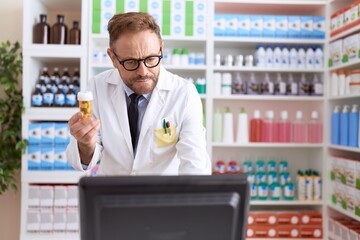 Middle age man pharmacist using computer holding pills bottle at pharmacy