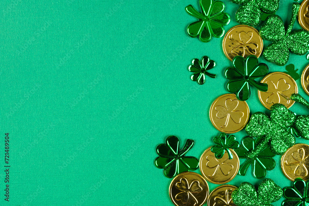 Poster St Patricks Day side border of  shiny shamrocks and gold coins. Top view over a green background with copy space.