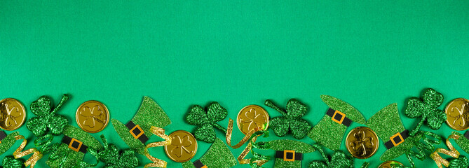 St Patricks Day bottom border of  shamrocks, leprechaun hats, gold coins and ribbon. Top view over...
