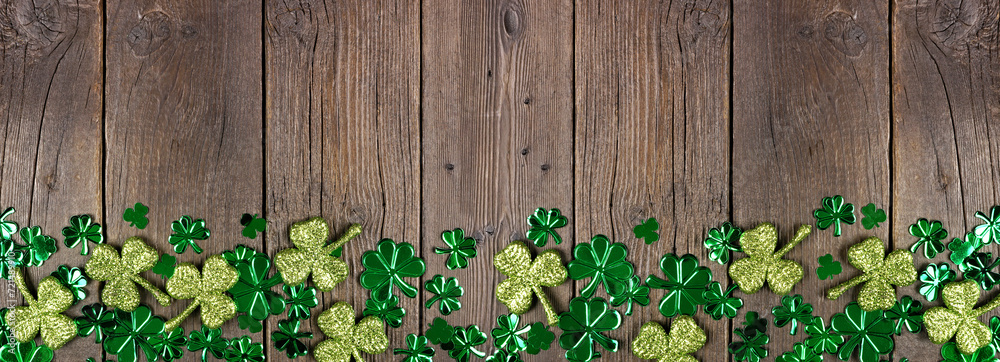 Poster St Patricks Day bottom border of  shiny shamrocks. Top down view over a rustic dark wood banner background with copy space.