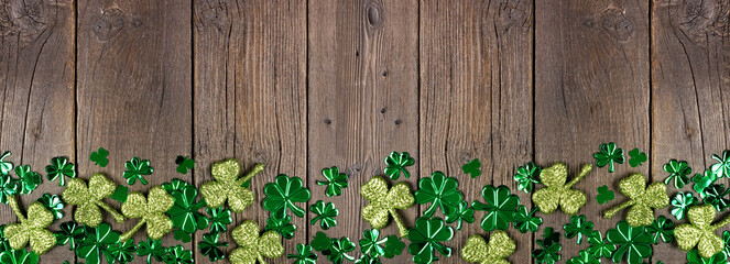 St Patricks Day bottom border of  shiny shamrocks. Top down view over a rustic dark wood banner...