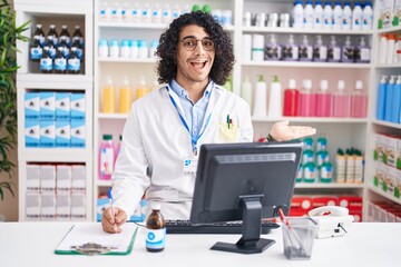 Hispanic man with curly hair working at pharmacy drugstore pointing aside with hands open palms...