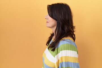 Middle age hispanic woman standing over yellow background looking to side, relax profile pose with natural face with confident smile.