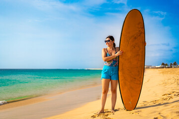 Beautiful woman holding surfboard standing on sunny beach Santa Maria, Sal island , Cape Verde
