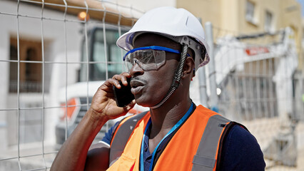 African american man builder standing with serious face talking on smartphone at construction place