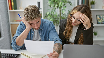 A stressed man and woman evaluate a document together in a modern office setting, conveying a sense...