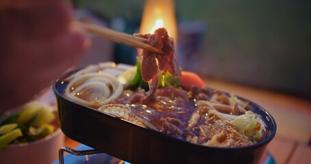 Close-up of a person enjoying a savory hot pot meal with chopsticks, with the warm glow of candlelight ambiance in the background
