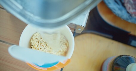 Overhead view of instant noodles being prepared with steaming hot water poured from an electric kettle, Hot water pouring into a cup of instant noodles, a quick meal preparation