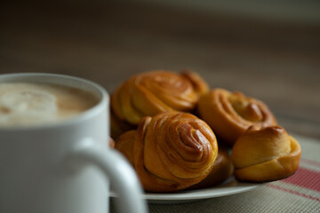 a cup of coffee and homemade buns on a plate.
