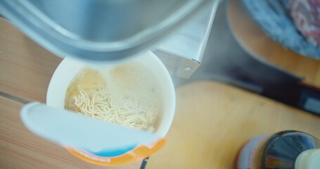 Overhead view of instant noodles being prepared with steaming hot water poured from an electric...