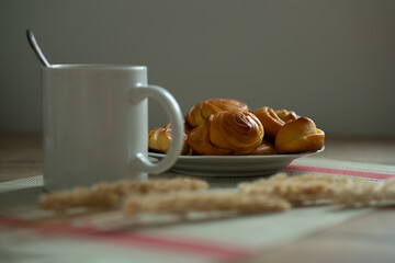 a cup of coffee and homemade buns on a plate, decorated with reed branches.
