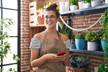 Young beautiful hispanic woman florist smiling confident using smartphone at florist - obrazy, fototapety, plakaty