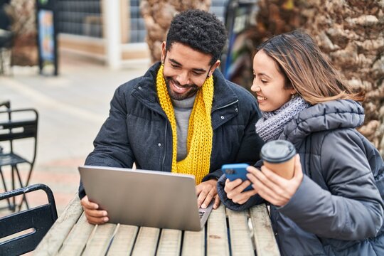 Man and woman couple using laptop and smartphone drinking coffee at coffee shop terrace