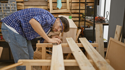 Handsome, serious, young arab man working diligently, sanding wood plank at the heart of his busy,...
