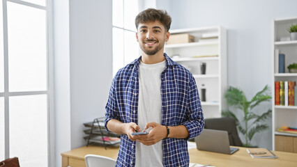 Confident young arab man, beaming with a happy expression, engrossed in work, effortlessly manages...